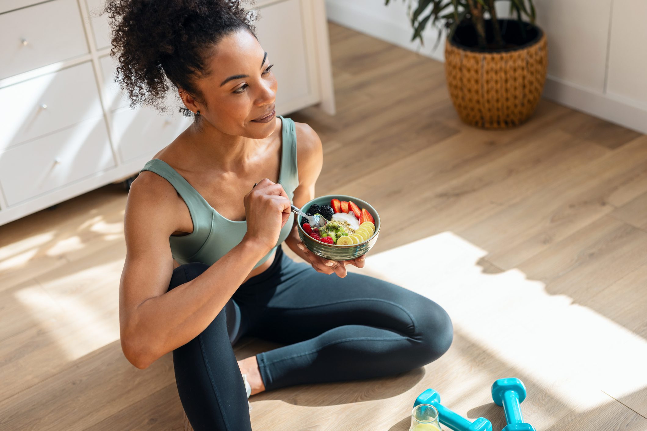 Woman enjoying a healthy meal while sitting on the floor after exercise.