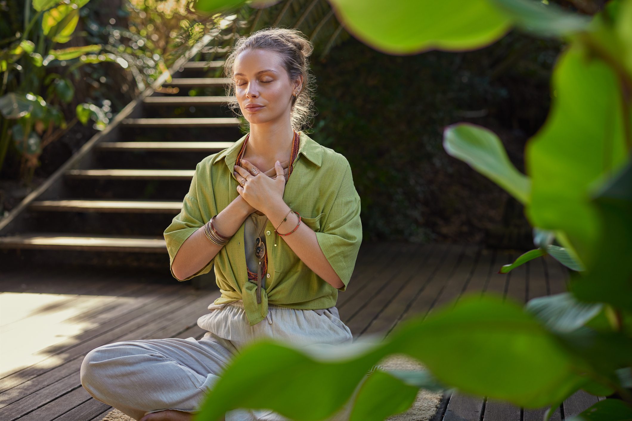 A woman meditates peacefully outdoors with hands crossed over her chest.