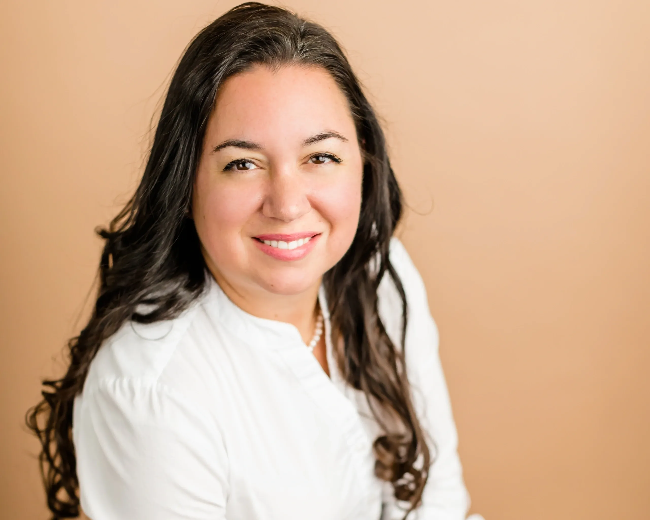 Smiling woman in white shirt, brown background.