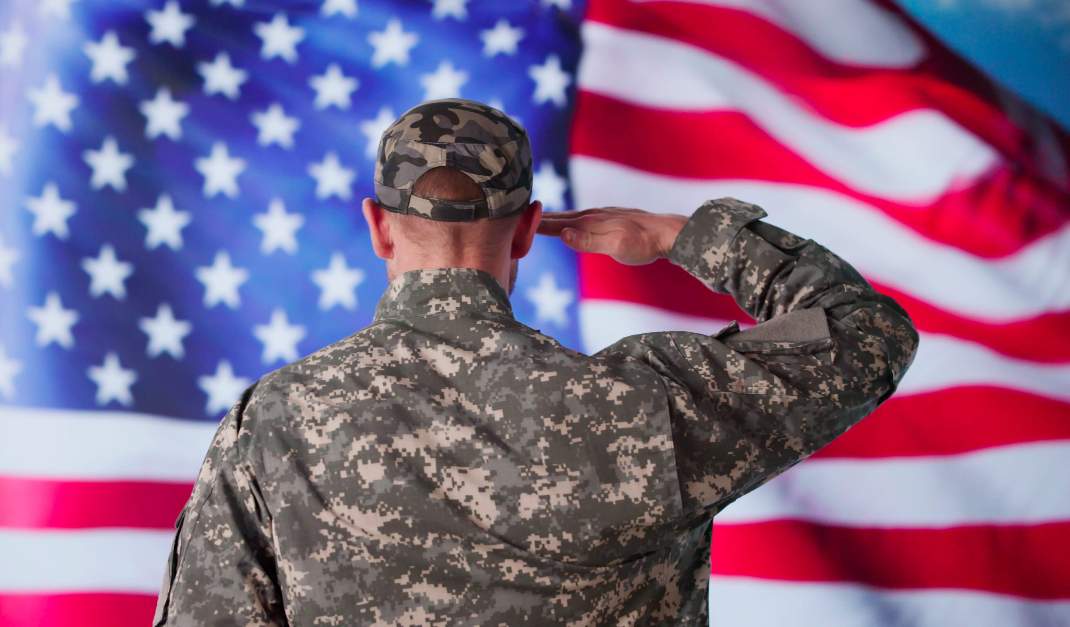 Soldier in camouflage saluting the American flag.