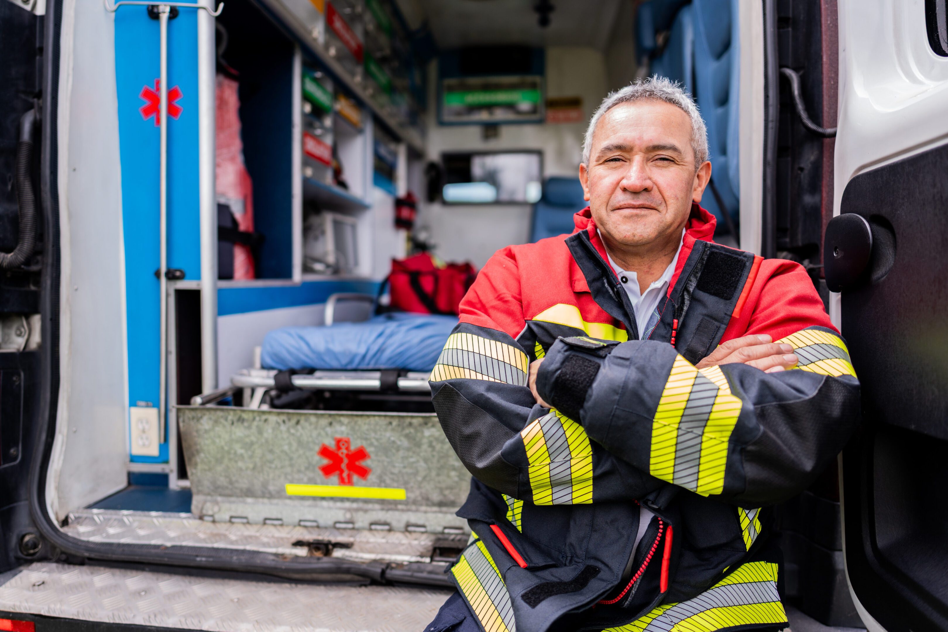 Confident firefighter posing in front of a fire truck with arms crossed.