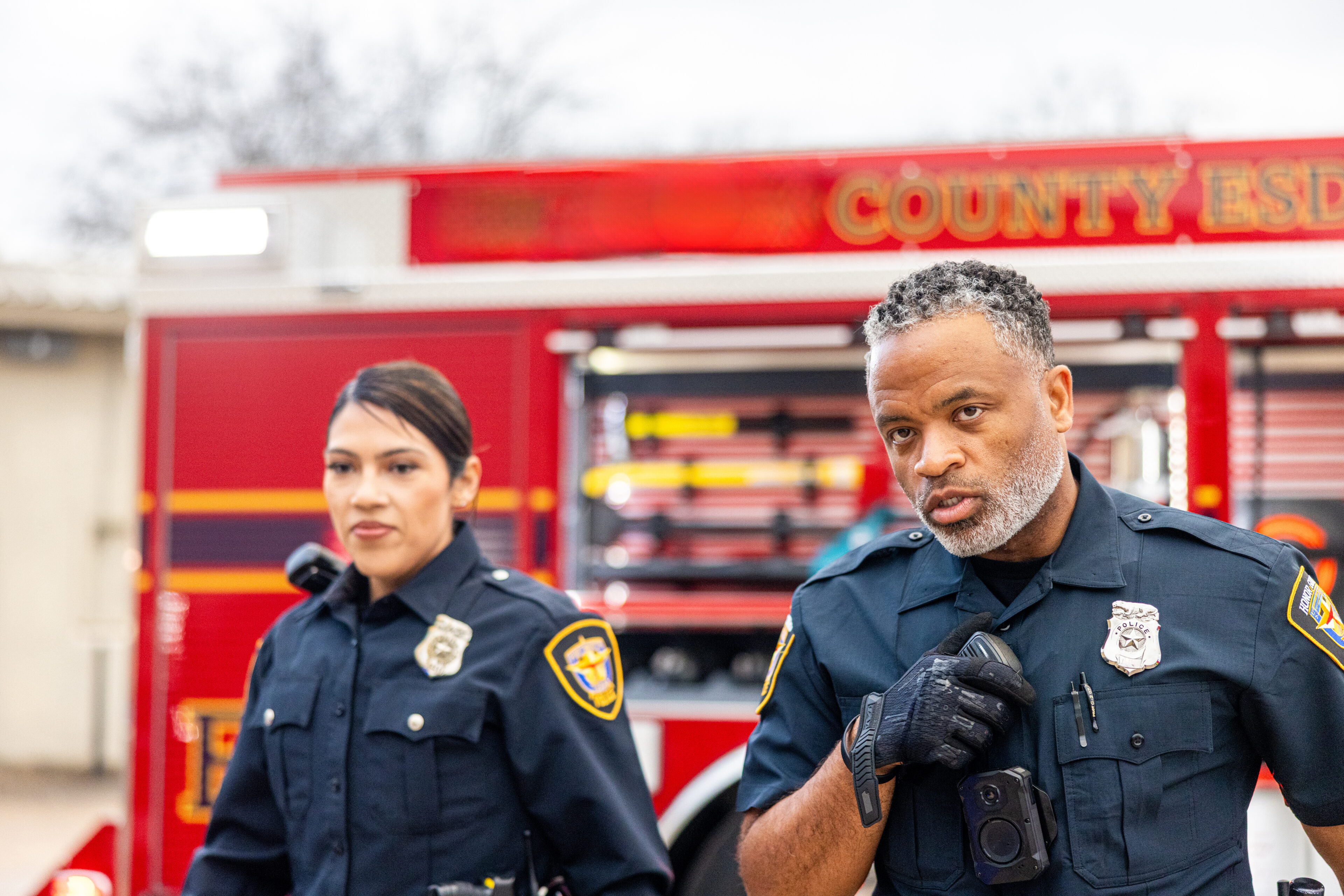 Two police officers standing in front of a fire truck, discussing something.