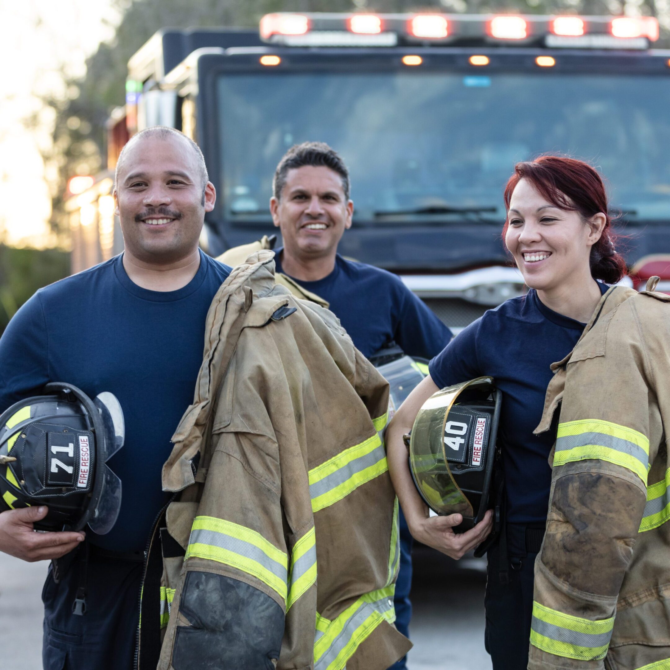 Three firefighters posing with gear in front of a fire truck.